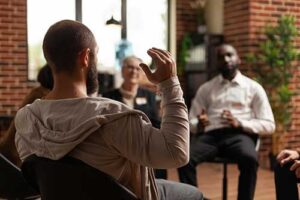 Man puts hand up to talk while in process addiction treatment