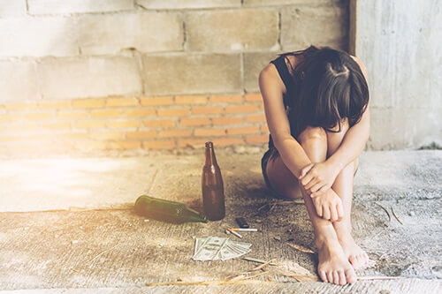 Woman sits on curb next to alcohol bottles