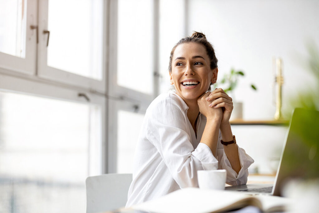 Woman smiles while sipping coffee and working at her laptop
