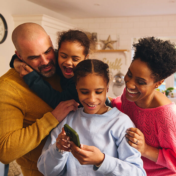 Family gathers around teen as she shows them pictures on phone