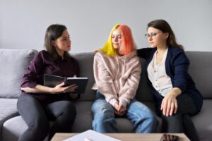 Two adults talking to a teen with orange and yellow hair