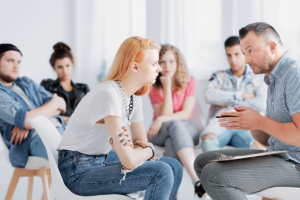 Man explaining something to a teen girl in a group therapy session