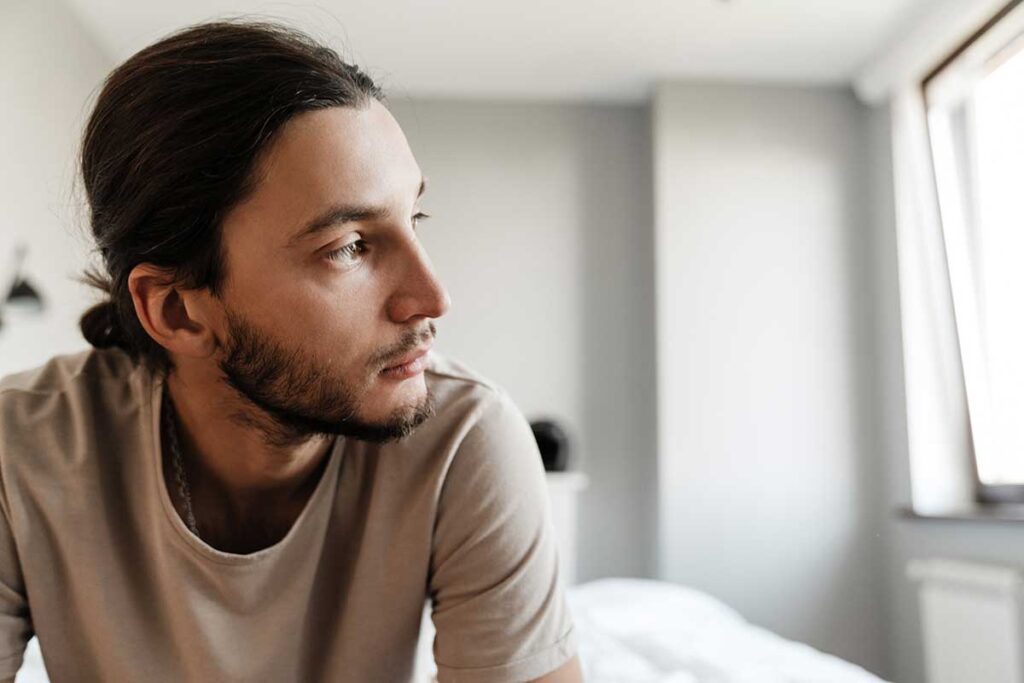 Man looks out window while pondering the long term side effects of Adderall