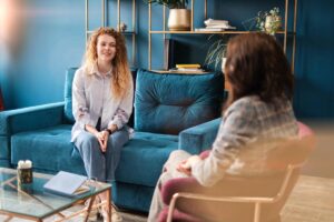 two women sitting in an office on a blue couch talking