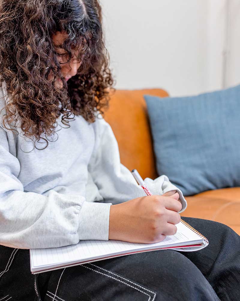 woman taking notes on a pad while sitting on a couch