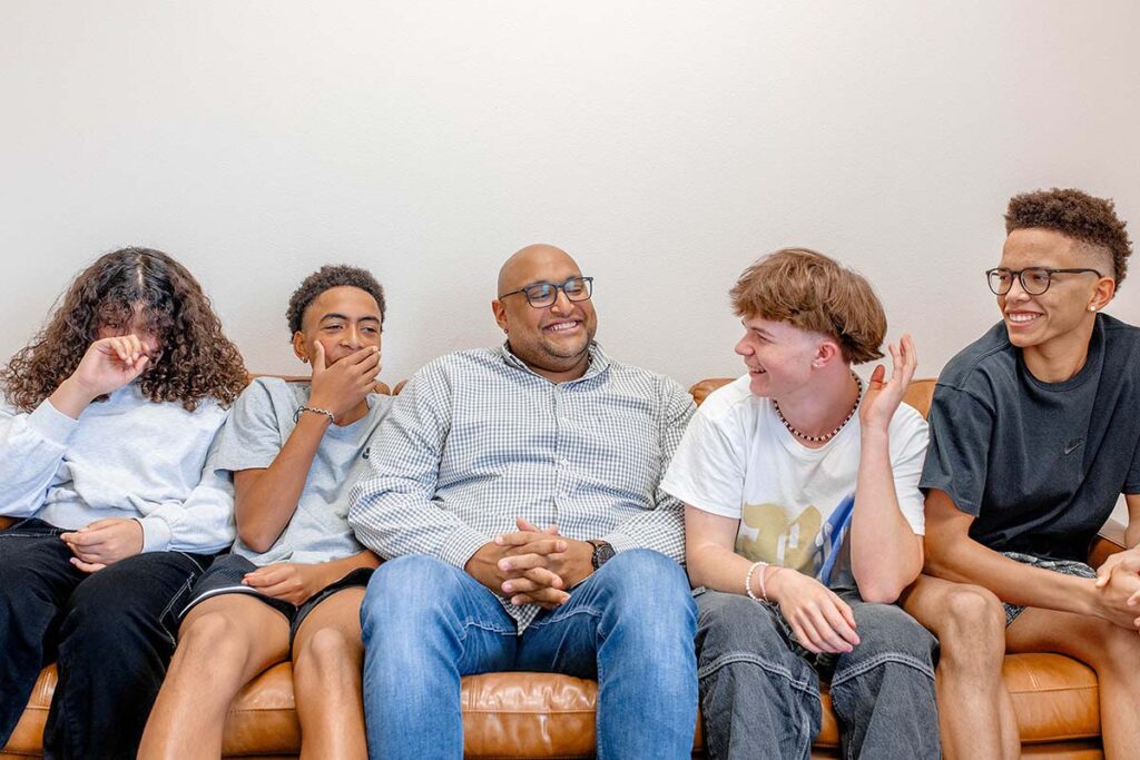 Group of adolescents smiling and talking to an adult on a couch