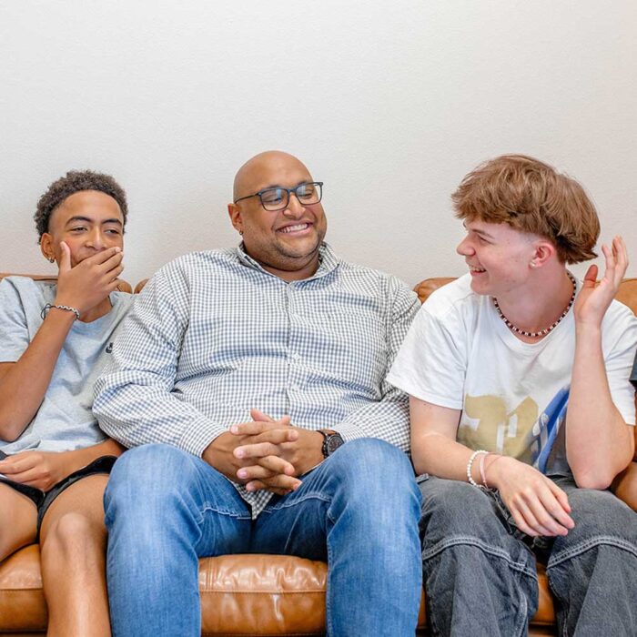 Two adolescents and an adult smiling together on a leather couch