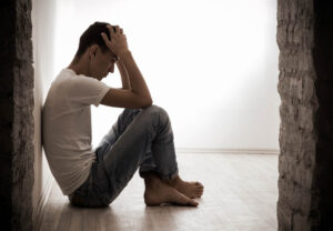 Man sits on floor pondering the difference between dependence and addiction