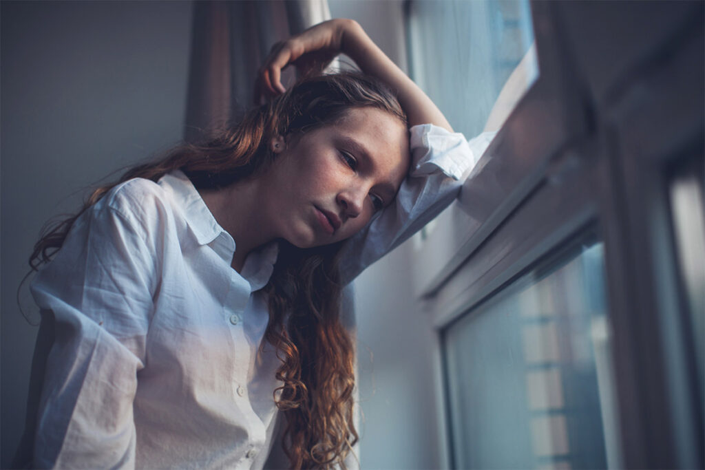 Teen leans on windows as she wonders how substance abuse affects children